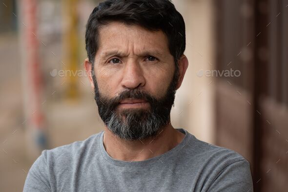 Bearded black-haired man, with a serious look, highlighting wrinkles on his face with frowning