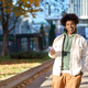 Smiling young African American teenager using phone standing at city street. - PhotoDune Item for Sale