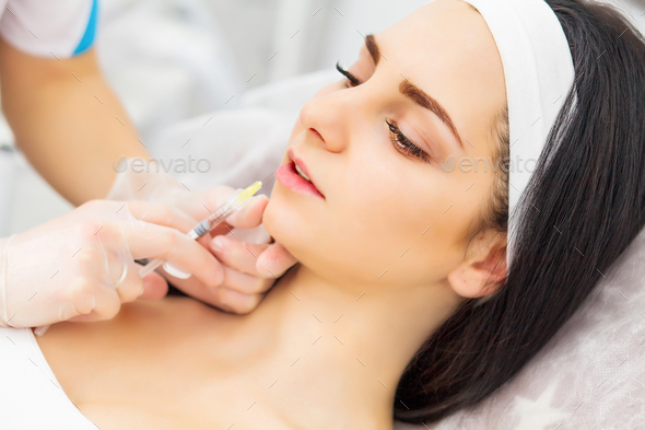 Close up of hands of cosmetologist making injection in female lips.