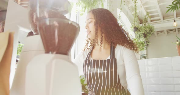 Happy biracial female barista making coffee using coffee machine at cafe alt