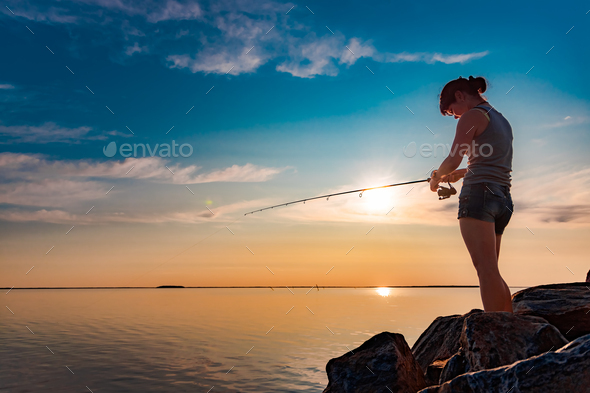 Woman fishing on Fishing rod spinning at sunset background. - Stock Photo - Images