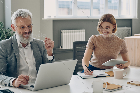 Two confident business people working together and smiling while sitting at the office desk - Stock Photo - Images