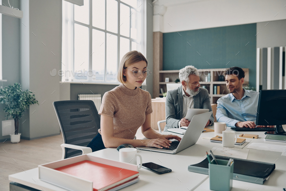 Group of confident business people working together while sitting at the shared desk in the office - Stock Photo - Images
