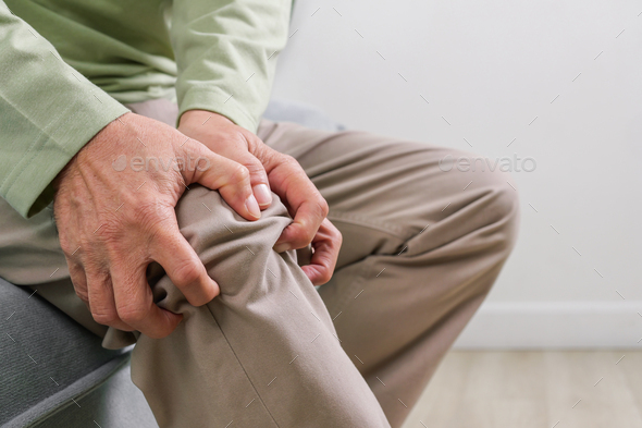 Elderly man suffering from knee pain sitting on sofa at home