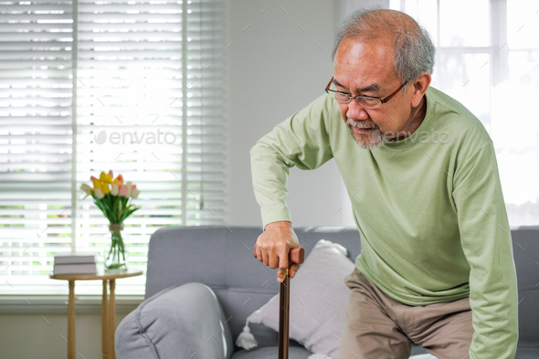 Senior man with health problems using walking stick to walk at home