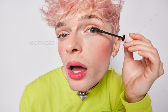 Close up portrait of transgender guy puts on makeup. Young gay man applies mascara on eyelashes