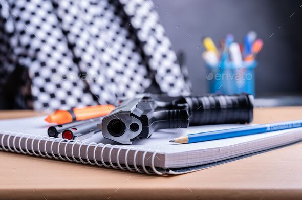 Closeup shot of school supplies and a gun on a table with blur background - gun regulation concept