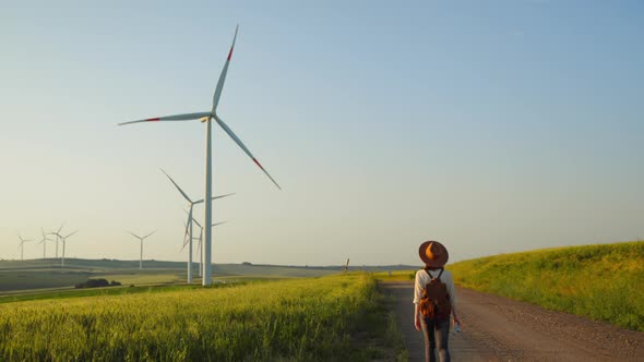 Attractive woman with a backpack in a field with eco windmills alt