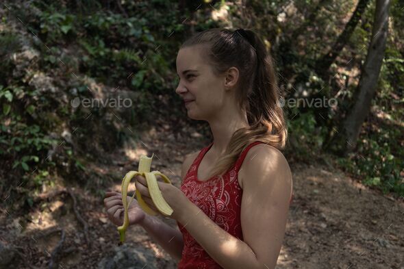 Shallow focus of a young female hiker eating a banana in the mountains in the countryside
