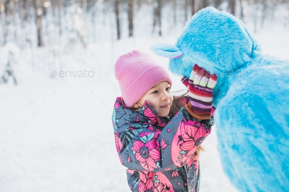 Closeup shot of a happy little girl pinching the cheeks of a female in a fluffy blue costume