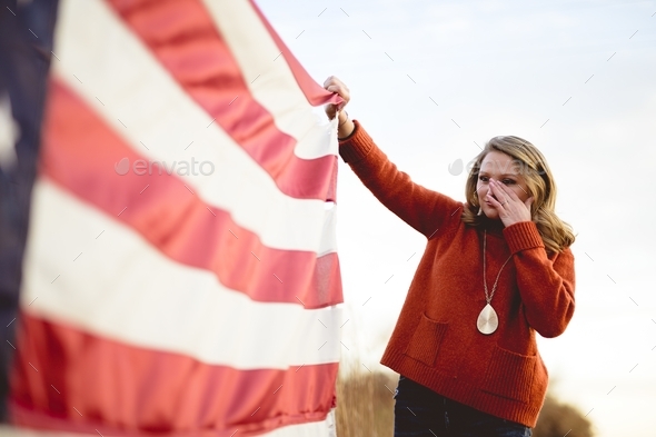 Female holding the flag of the United States while rubbing his eyes
