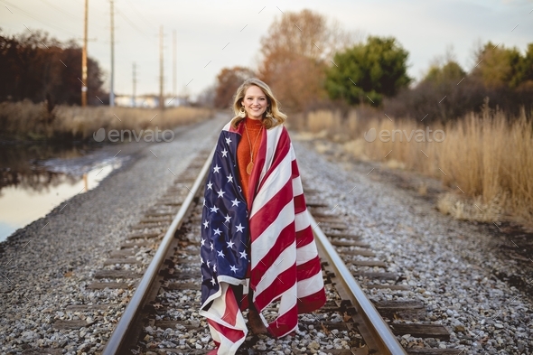 Smiling female holding the United States flag while walking on the train rails