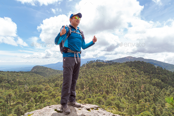 Hiker standing on the edge of a cliff with a thumbs-up gesture and a beautiful nature scene behind