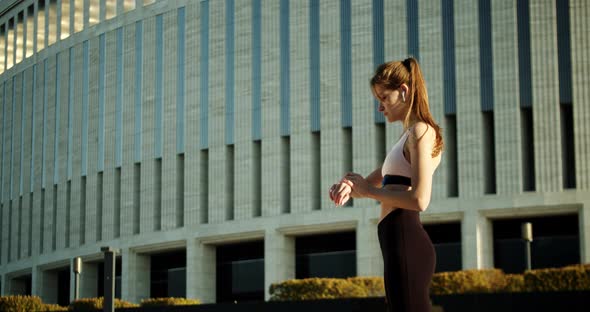 Young Woman Uses Smart Watch and Headphones Before Jogging