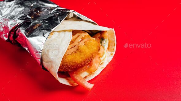 Closeup of chicken wing wrap rolled in tin foil on a red background