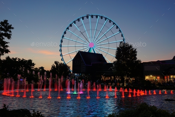Ferris wheel and water fountain with colored lights at dusk
