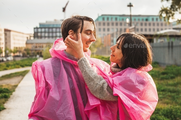 Closeup shot of a male and female in pink plastic raincoats romantically looking at each other