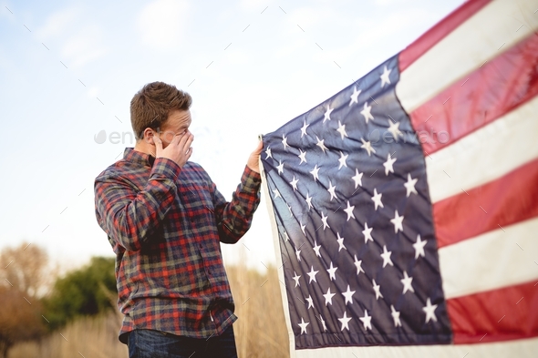 Male holding the flag of the United States while rubbing his eyes