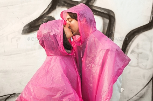 Closeup shot of a male and a female in pink plastic raincoats kissing each other