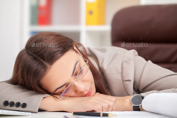 Young tired woman at office desk sleeping with eyes closed, sleep deprivation