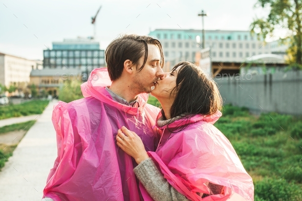 Closeup shot of a male and a female in pink plastic raincoats kissing each other