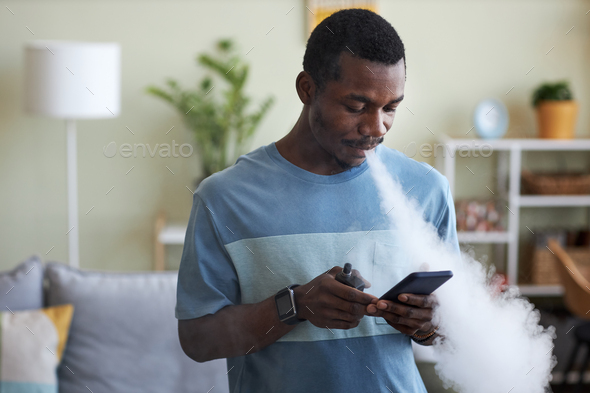 Young African American businessman scrolling in smartphone and smoking