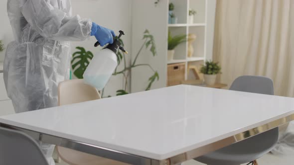Slowmo of Woman in Protective Suit Disinfecting Table Surface alt