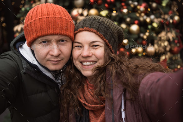 Close up positive couple in love wearing hats and winter clothes at christmas tree background - Stock Photo - Images