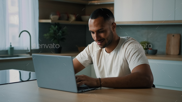 African millennial man multiracial guy American male user freelancer sitting at home kitchen desk - Stock Photo - Images