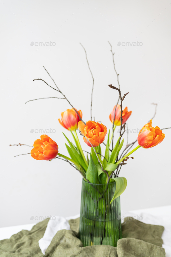 A very beautiful spring bouquet in a green vase stands on a table on a linen tablecloth, orange