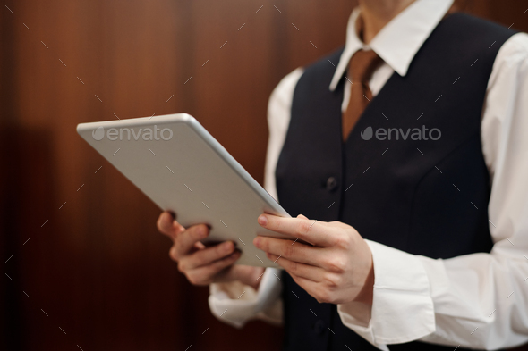 Close-up of young female staff of hotel using tablet by workplace
