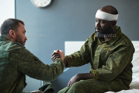 Young soldier shaking hand of African American friend with injured head