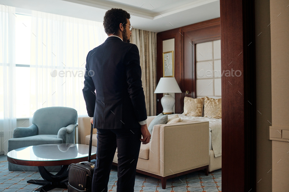 Rear view of white collar worker in elegant suit entering room of luxurious hotel