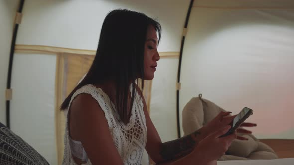 Portrait of a Pretty Asian Woman Using Her Mobile Phone Inside the Tent House alt