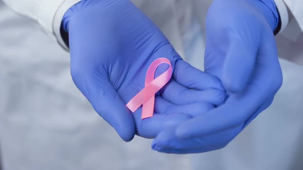 Hands in Gloves Carefully Holds Pink Ribbon, Symbol of Breast Cancer Awareness alt