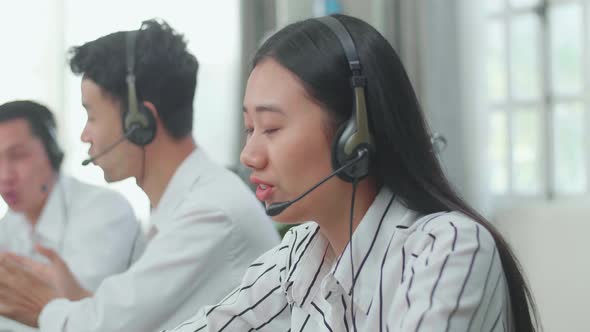 A Woman Of Three Asian Call Centre Agents Speaking To Customer While Her Colleagues Are Talking alt