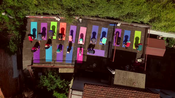 Aerial view of a group of people doing yoga on a terrace surrounded by trees. alt