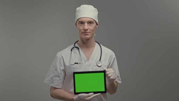 Young Doctor In Medical Gown And Gloves He Holds Tablet alt