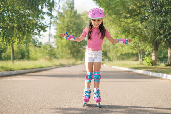 Preschool girl in protective helmet and roller skates rides on asphalt path