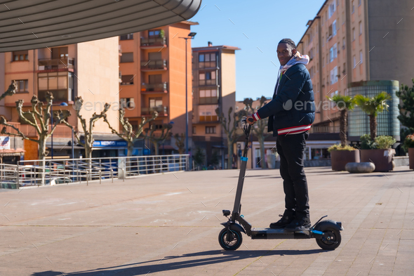 Black ethnic male skateboarding on an electric skateboard, green and clean mobility