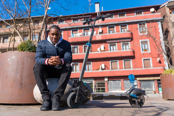 Portrait of black ethnic male skateboarding on an electric skateboard in the city, new mobility