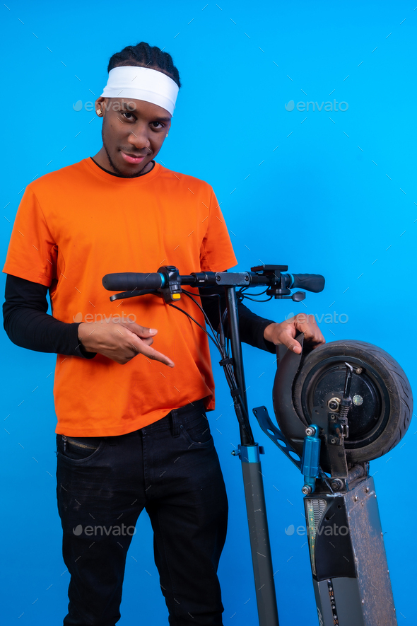 Portrait of a black ethnic man in orange clothes on a blue background, with an electric skateboard