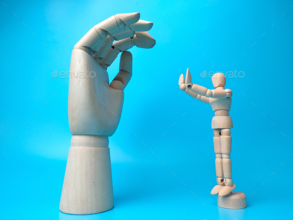 A wooden mannequin makes a pose holding a wooden hand on a blue background - Stock Photo - Images