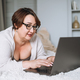 Smiling middle aged plus size woman lying on bed, working on laptop from home - PhotoDune Item for Sale