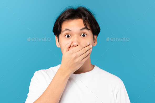 Shocked Chinese Guy Covering Mouth With Hand On Blue Background