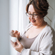 Smiling middle aged plus size woman with day cream near window at home - PhotoDune Item for Sale
