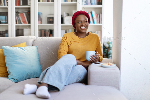Cheerful happy black woman chilling alone on couch at home