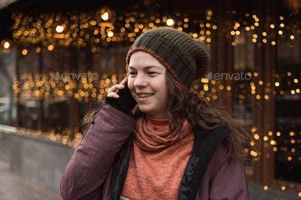 Happy woman in winter clothes talking on mobile phone outdoors at lights of garlands background - Stock Photo - Images