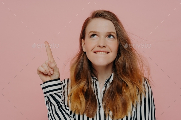 Young woman thinking while biting lips and having pointer finger up