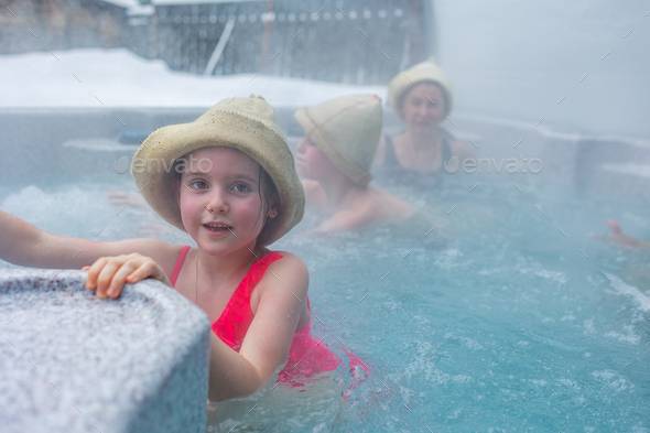 Cheerful happy family with children enjoys hot bath in jacuzzi whirlpool on cold winter day